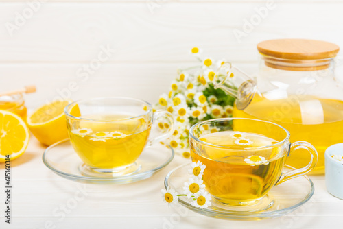 Chamomile herbal tea in a glass cup on a white wooden table with honey, lemon and chamomile bouquet. Close-up. Copy space. Useful herbal drinks, immunity tea. Natural healer concept.Place for text.