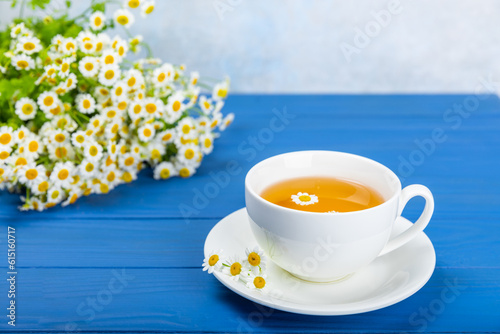 Fototapeta Naklejka Na Ścianę i Meble -  Chamomile herbal tea in a cup on a blue wooden table with honey, lemon and chamomile bouquet. Close-up. Copy space. healthy herbal drinks, immunity tea. Natural healer concept.Place for text.