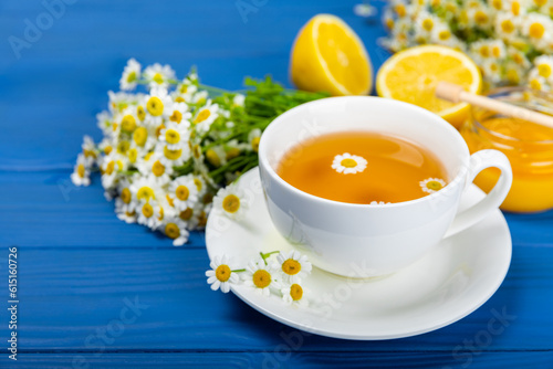 Chamomile herbal tea in a cup on a blue wooden table with honey, lemon and chamomile bouquet. Close-up. Copy space. healthy herbal drinks, immunity tea. Natural healer concept.Place for text.