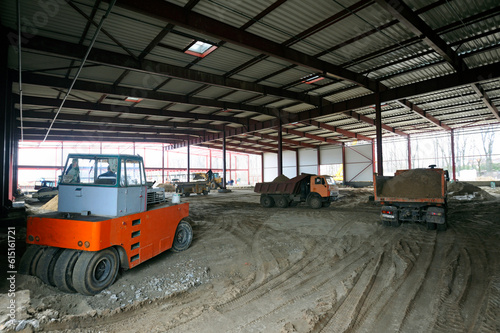 Construction site of a hangar building, an excavator and dump trucks loaded © Yurii Zushchyk