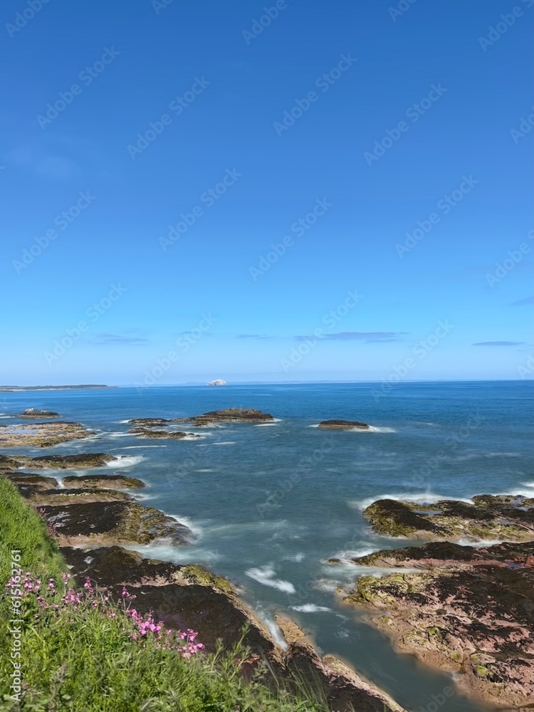 Ocean view with waves crashing onto rocks and a clear blue sky background. Dunbar Scotland. 