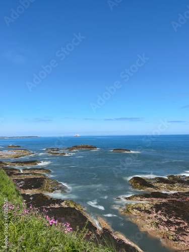 Ocean view with waves crashing onto rocks and a clear blue sky background. Dunbar Scotland. 