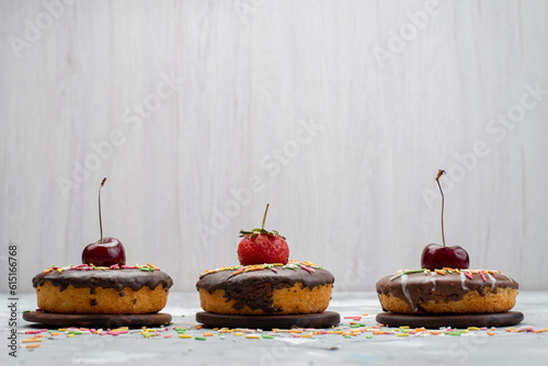 a front view little chocolate donuts with designed fruits on top on the grey background sweet sugar cake fruit chocolate