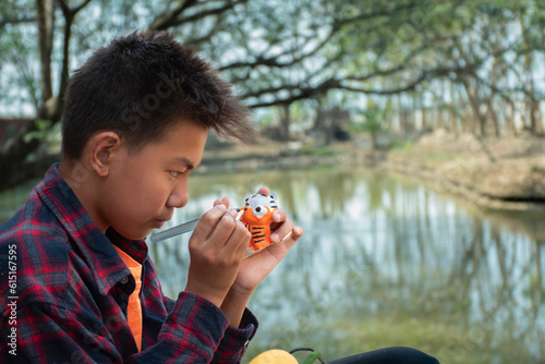 Young asian boy in plaid shirt sitting by the pond in the backyard and spending his free time by drawing, coloring and fixing his fruit and animal models sculpted from plaster with watercolor happily. #615167595