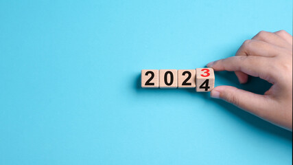 2024 Happy New Year eve wooden blocks flip change hand blue background. Countdown starting ending 2023 action schedule calendar strategy future vision. Business startup plan resolution celebration