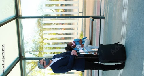 Vertical view on multietchic people waiting transport at bus station. Businessman with elegant suit holding bagcase. People wearing protective facial masks. Spread of coronavirus infection. photo