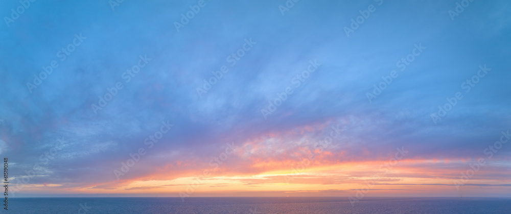 Aerial, panoramic view of the colourful blue, pink and red coloured evening sky over the sea with no obstacles in front. Ideal for sky replacement projects.