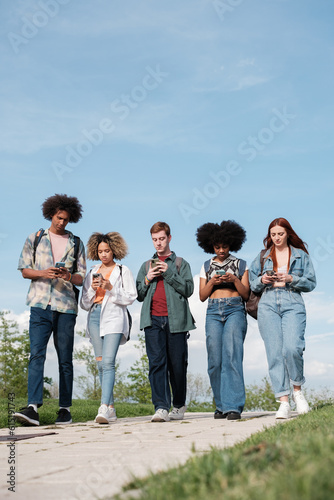 Group of university students walking around the campus looking at their mobile phones. Concept: technology, addiction, youth