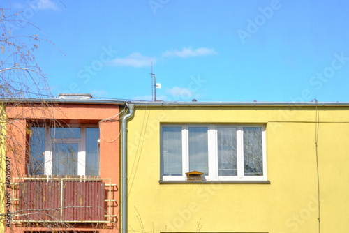 Window with a nest box birdhouse and balcony of thermally insulated colorful weatherized block of flats apartment building, surrounded with trees under clear blue sky. Generic building detail. © Artem