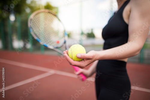 Sports girl is preparing to serve a tennis ball. Close-up of a beautiful young girl holding a tennis ball and racket. © Tania