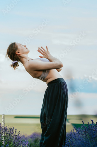 Woman in palazzo pants and top doing yoga backbend with namaste hands in rural lavender field photo