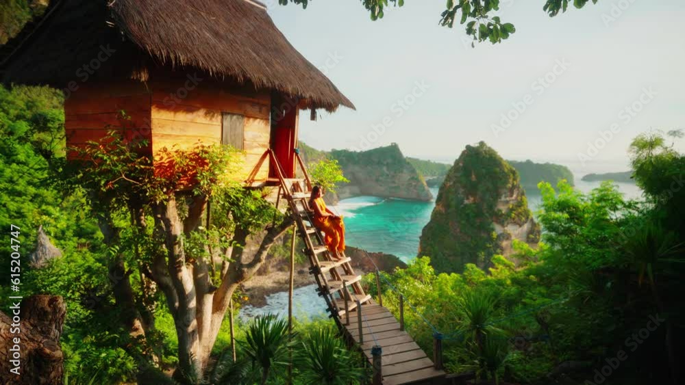 Silhouette beautiful travel girl in dress rising to a picturesque tree hut on top mountain cliff on background tropical beach and scenery rocks in ocean 4K
