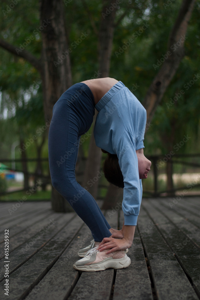 View on young girl in blue gym suit is doing acrobatics exercises in rainy weather in the park