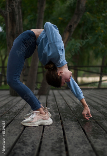 Young girl with athletic body is doing acrobatics exercises in rainy cloudy weather in the park © Veronica Holubnycha