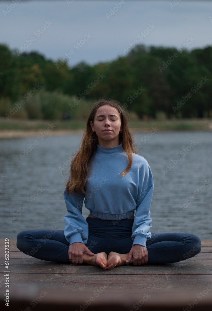 View on a girl in Lotus Pose near lake in cloudy rainy weather