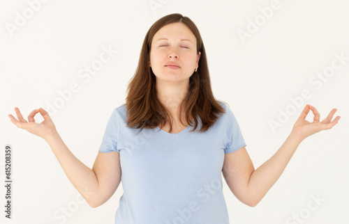 Mindful caucasian pregnant woman meditates indoor, keeps hands in mudra gesture, has eyes closed, tries to relax after long hours of working, holds fingers in yoga sign, isolated on white wall