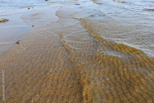 Transparent water with sun glare and ripples on sandy bottom. Sea waves and gritty surface texture created a pattern of dunes on the  floor of sea beach.