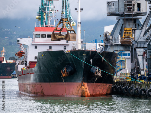 Cargo freight ship loading by bucket crane in industrial harbor or port terminal. Trade logistic, import and export concept.