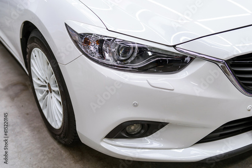 Protective film sticker on the headlight of a white car. Car detailing studio © thomsond