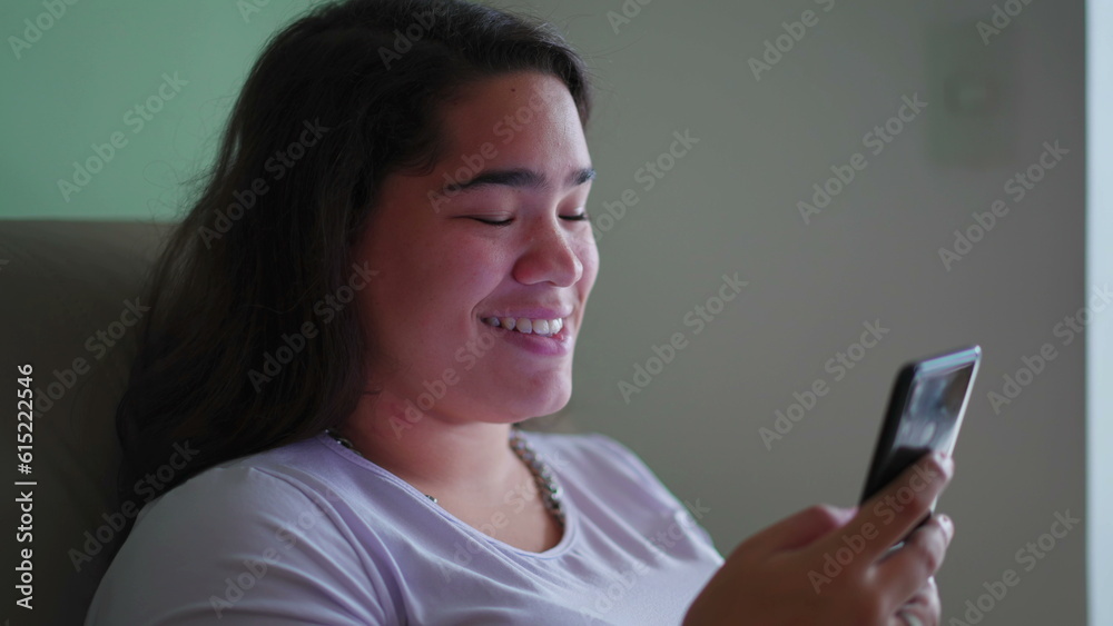 Happy Brazilian Teen Girl Reacts Positively to Online Content, Holding Phone. Candid scene of a Diverse Asian woman Smiling as She Reads Message Happy Brazilian Teen Girl Reacts Positively to Online Content, Holding Phone. Candid scene of a Diverse Asian woman Smiling as She Reads Message