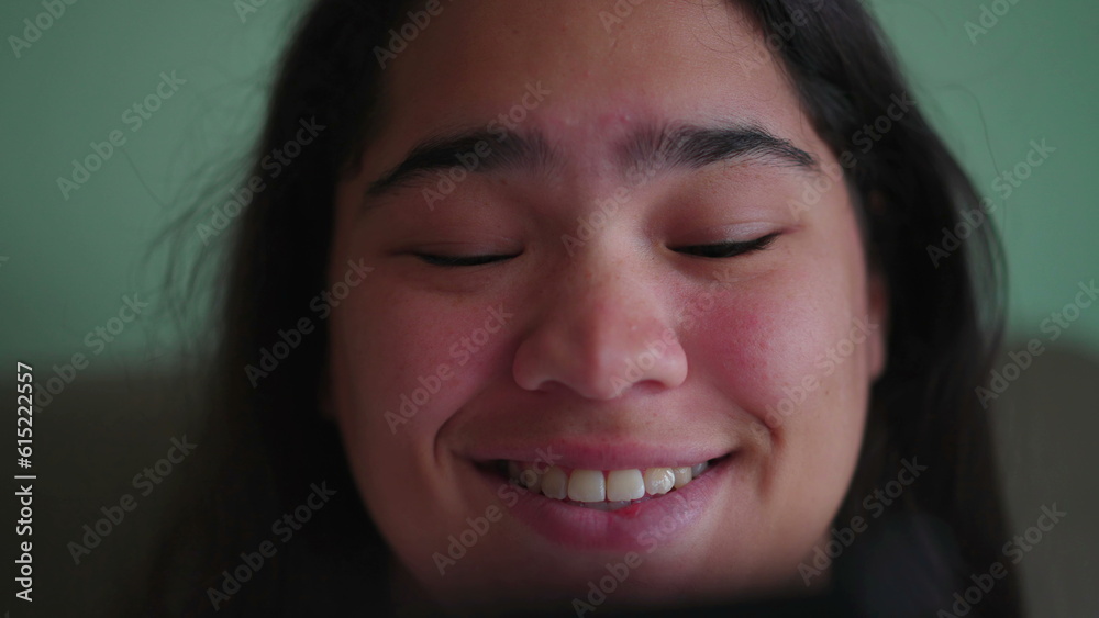 Joyful Brazilian teen girl react_s positively to content online while holding phone. Close-up of a happy diverse Asian woman_s face smiling reading message Joyful Brazilian teen girl react_s positively to content online while holding phone. Close-up of a happy diverse Asian woman_s face smiling reading message