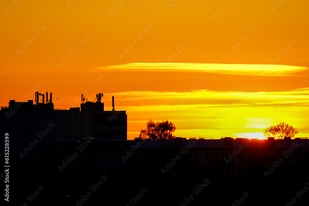 Colorful sunset in city, silhouettes of houses on the background of a golden sunset