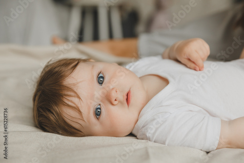 Charming blue-eyed 6-month-old baby lies in bed in a white bodysuit. View from above photo