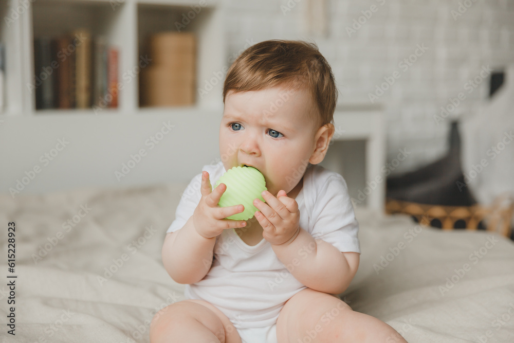 Baby 6 months old gnaws the ball, holding it with his hands, sitting on the bed. teething. Baby 6 months old gnaws the ball, holding it with his hands, sitting on the bed. teething.