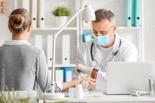 Mature male doctor taking patient's pulse in clinic