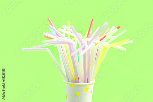Paper cup with different colorful straws on green background