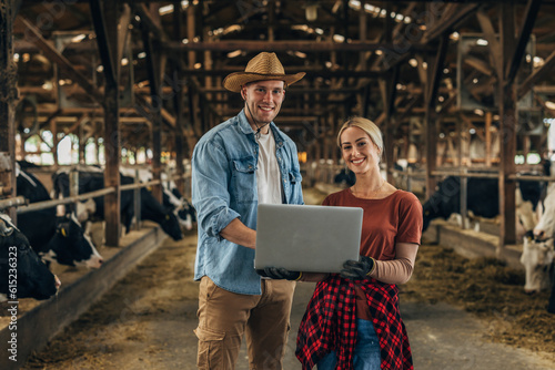 Man and woman holding laptop in a stable and looking at the camera.