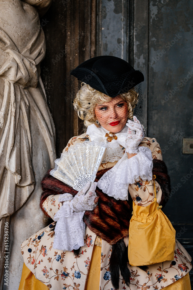 Venice, Italy, 11 February 2023: Colorful carnival masks at famous traditional festival on Saint Mark's Square at sunset, Elegant Venetian Costume, historical dress with embroidery and hat with veil