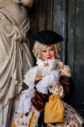 Venice, Italy, 11 February 2023: Colorful carnival masks at famous traditional festival on Saint Mark's Square at sunset, Elegant Venetian Costume, historical dress with embroidery and hat with veil