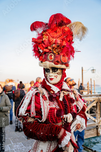 Venice, Italy, 11 February 2023: Colorful carnival masks at famous traditional festival on Saint Mark's Square at sunset, Elegant Venetian Costume, red velvet dress with embroidery and feathers © AnnaRudnitskaya