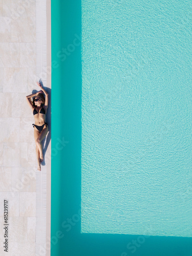 a girl in a black swimsuit lies by the pool. view from a copter.