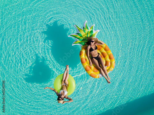 Aerial drone view of girls in swimming pool from above, happy kids swim on inflatable ring donut and mattress, girls have fun in water on family vacation on holiday resort