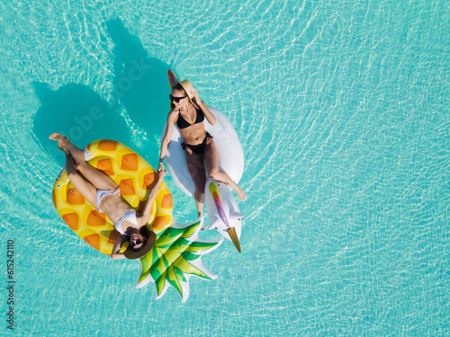 Top view of female friends wearing bikini lying on an inflatable toy in pool. Woman sunbathing on floating pool inflatable toy.