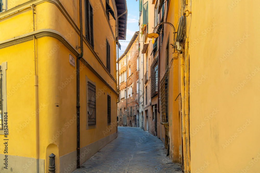 A narrow curving alley surrounded by yellow stucco residential buildings in the historic medieval old town of Lucca, Italy, in the Tuscany region.