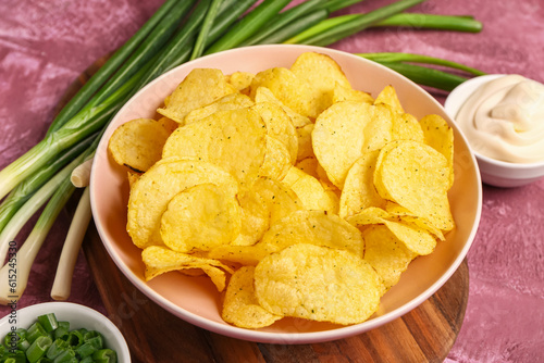 Bowls of tasty sour cream with sliced green onion and potato chips on purple background