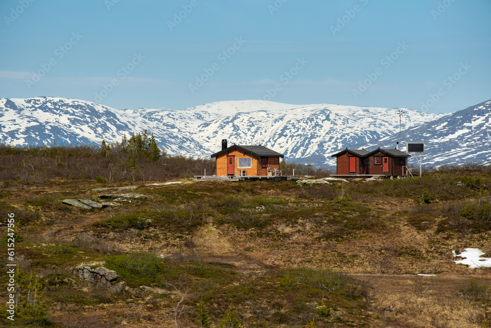 Mountain cabin on Risfjellet, Mo i Rana, Norway. Norwegian mountain landscape in early summer with snow on the high mountain peaks. Pine trees and high altitude. Mountain lake, fjord. Lone cabins