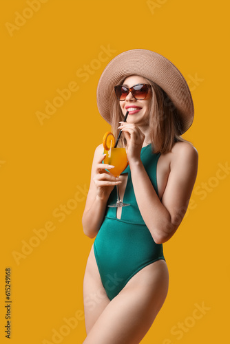 Young woman in swimsuit drinking cocktail on yellow background
