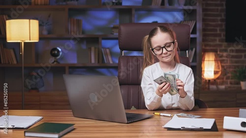 Pretty caucasian female child spending evening in parents' office with laptop and counting dollar banknotes. Happy girl feeling satisfied with financial income and clutching money to chest. photo
