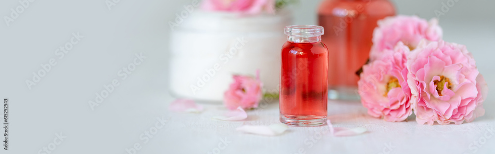 Composition with pure natural organic rose essential oil in glass bottle, luxury perfumery ingredient for fragrance, skin care products, anti-age beauty treatment. Fresh flowers banner copy space text