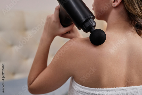 Closeup of young woman using massager for back and shoulders at home, copy space