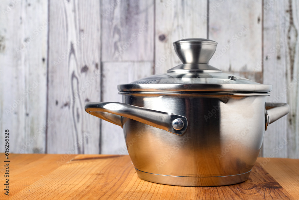 Stainless steel saucepan with a glass lid on a wooden table. Side view. Stainless steel saucepan with a glass lid on a wooden table. Side view.