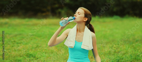 Fitness portrait of young sportswoman drinking water from bottle in summer park