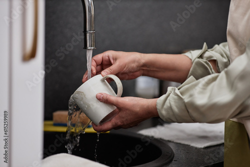 Closeup of unrecognizable woman washing coffee mug in tap water in kitchen, copy space