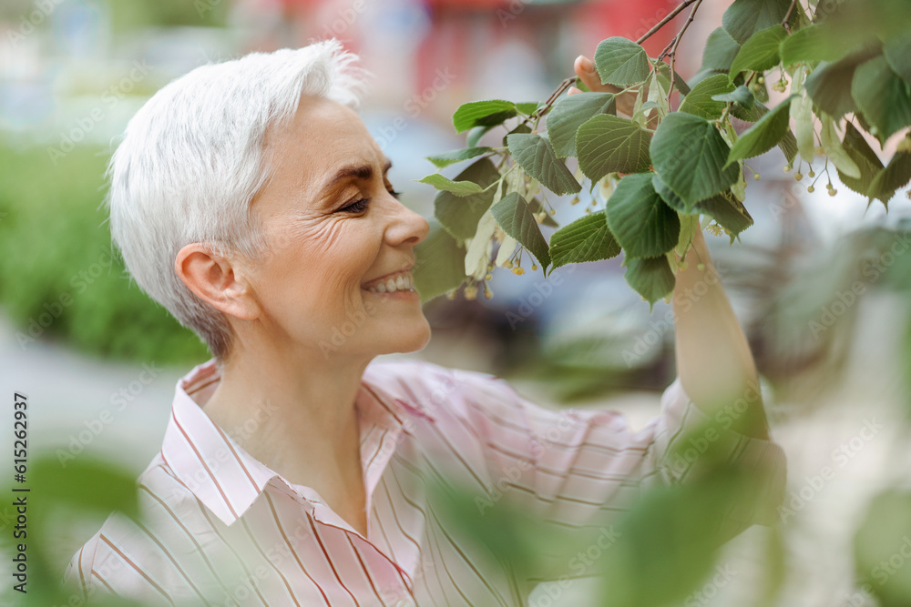 Portrait of smiling senior woman sniffing flowers aroma with closed eyes on the street