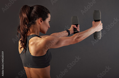 Female sporty muscular young serious woman doing strength workout on the shoulders, biceps and arms in sport bra holding dumbbells on black background with empty space. Closeup
