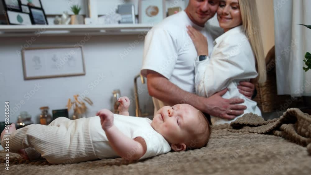 Beautiful Caucasian couple stand close to each other. Happy smiling people look at the baby lying at the table beside them. Beautiful Caucasian couple stand close to each other. Happy smiling people look at the baby lying at the table beside them.